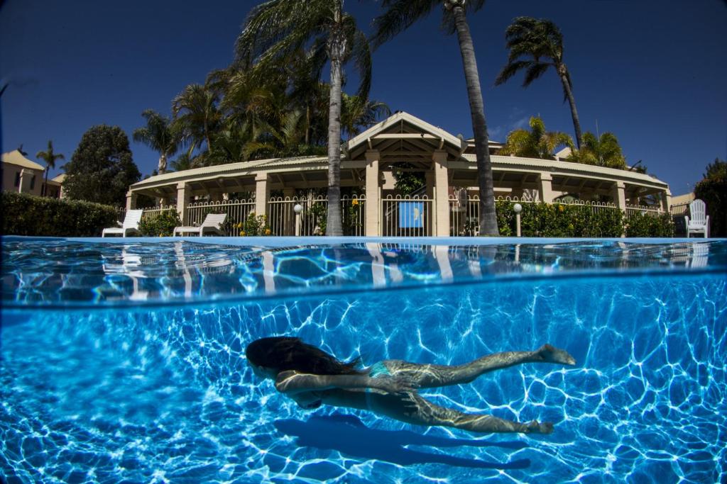 Woman swimming underwater in a crystal-clear pool at a tropical Kalbarri resort surrounded by palm trees.