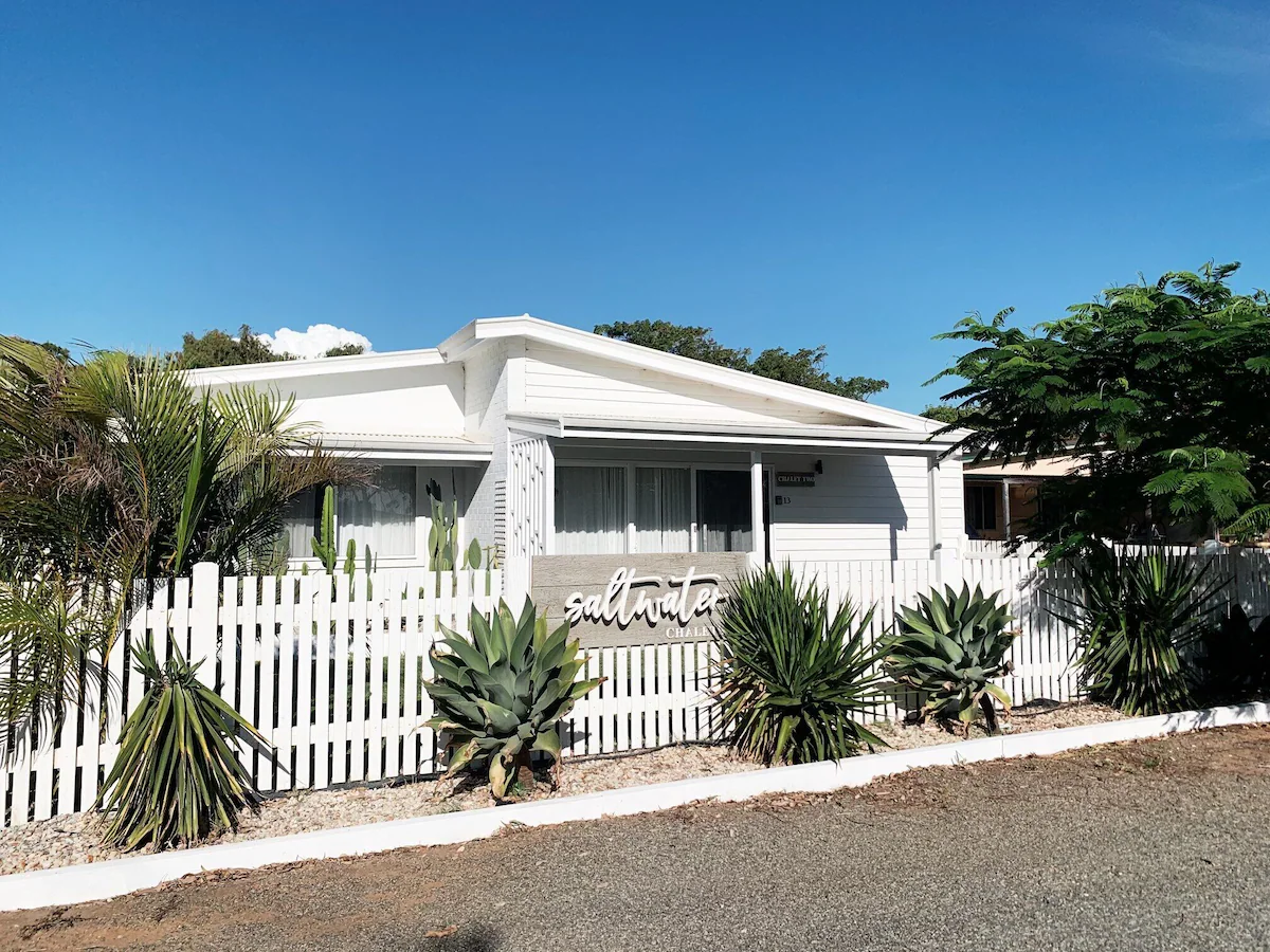 Saltwater Chalet 2 in Kalbarri, a stylish white holiday home with a picket fence and lush greenery
