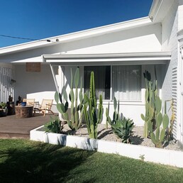 Exterior view of Saltwater Chalet 1 in Kalbarri, featuring a modern white facade, cactus garden, and outdoor seating.