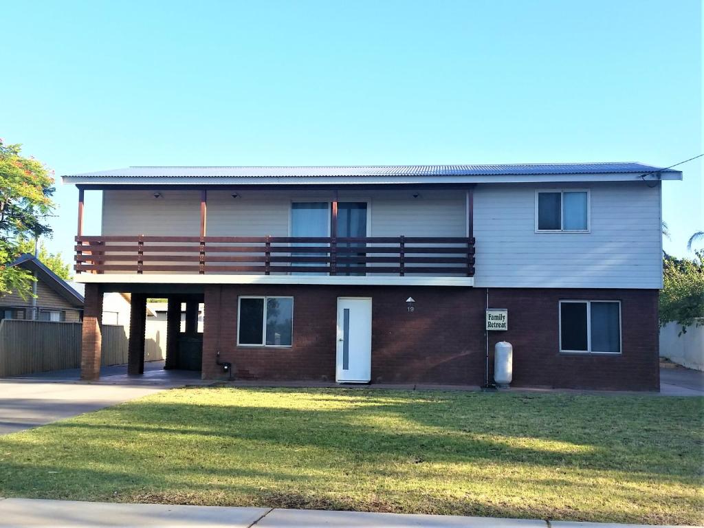 Double-storey holiday home with brick base, upper balcony, and wide driveway, set on a grassy front yard under a clear sky.