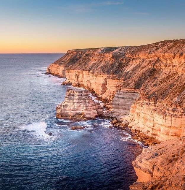 Sunset lighting up the dramatic limestone cliffs of Kalbarri’s coastline, with the Indian Ocean waves crashing below.