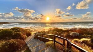 Sunset over the Indian Ocean from the Jakes Point boardwalk in Kalbarri, Western Australia, with golden light reflecting off the waves and native coastal vegetation.